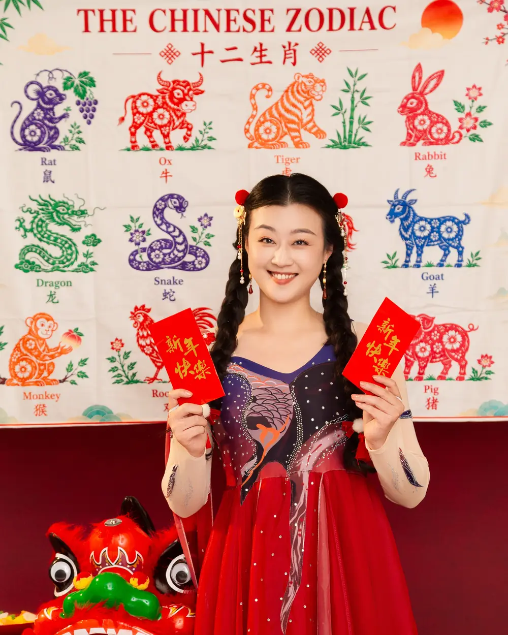 Raina holding two lucky red envelopes in front of a Chinese zodiac backdrop