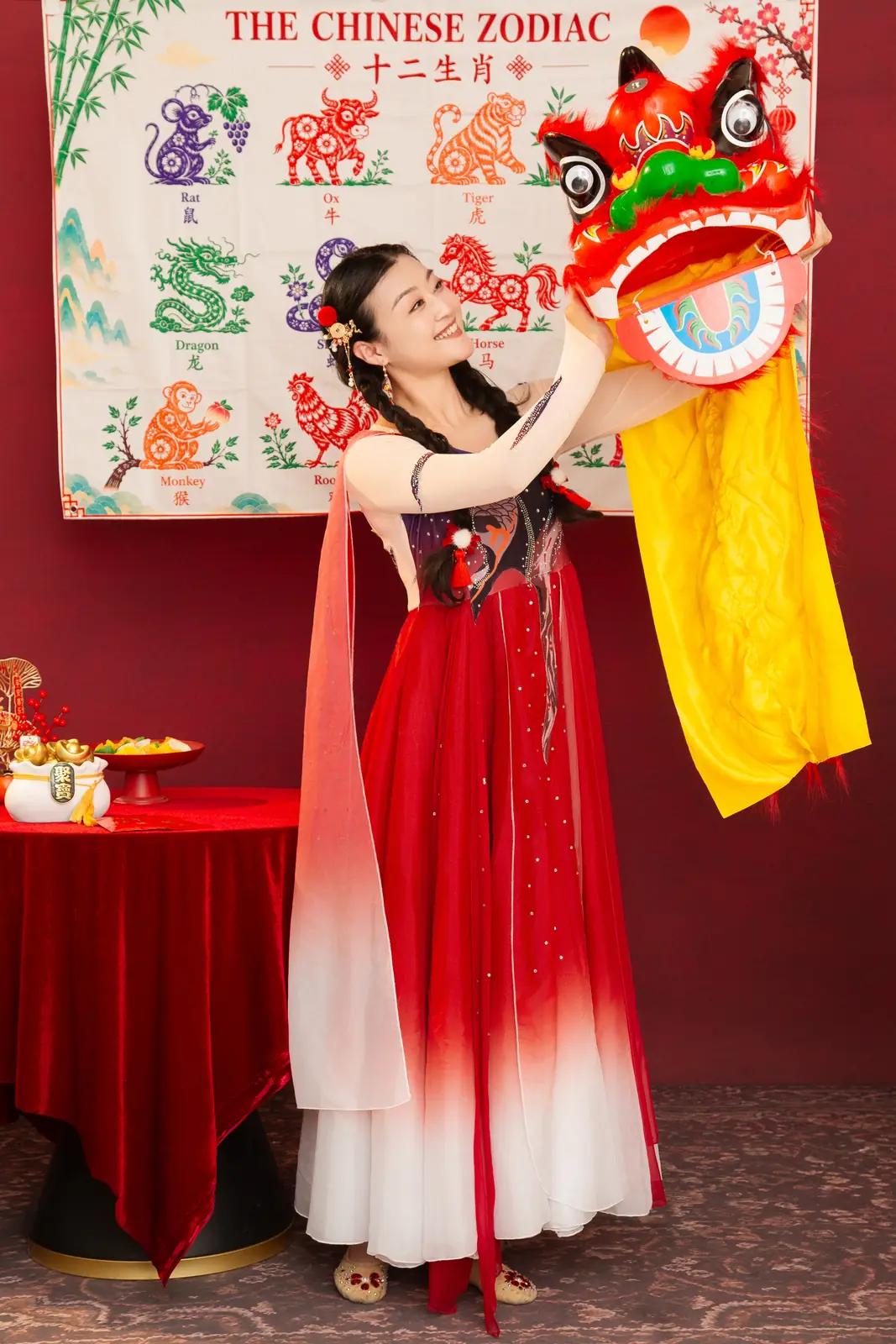 Raina lifting a lion dance head in front of a Chinese zodiac backdrop