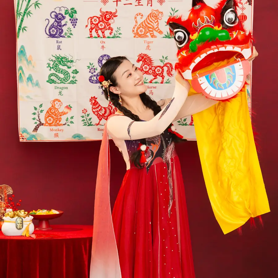 Raina lifting a lion dance head in front of a Chinese zodiac backdrop